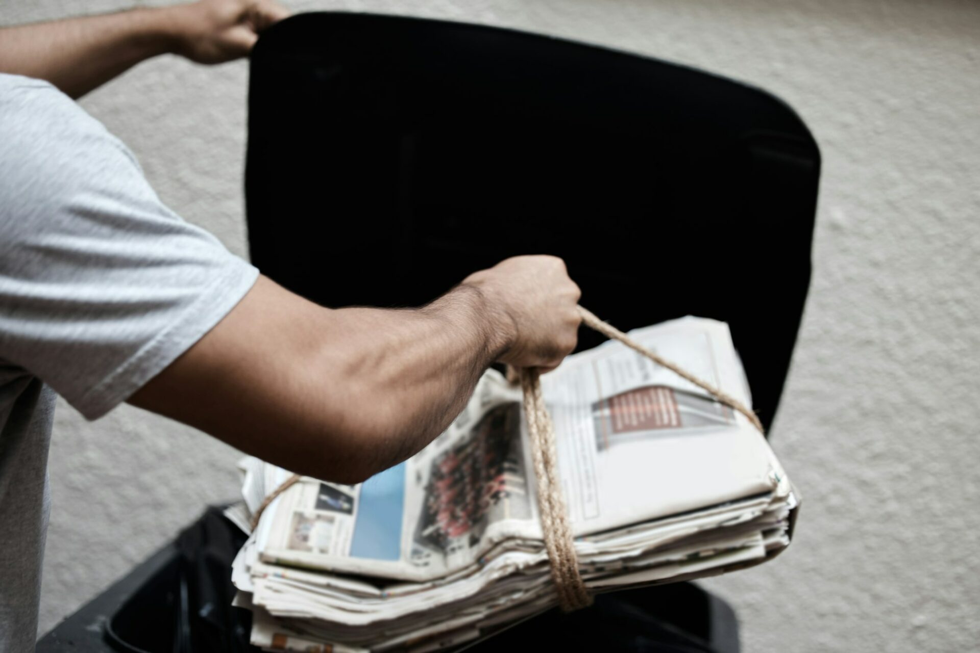 Shot of a young man putting newspaper in the bin to be recycled